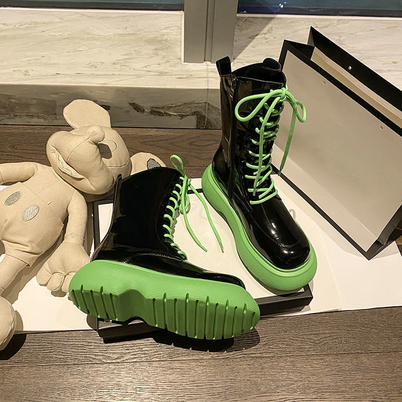Black boots with green soles on a wooden floor next to a plush toy.