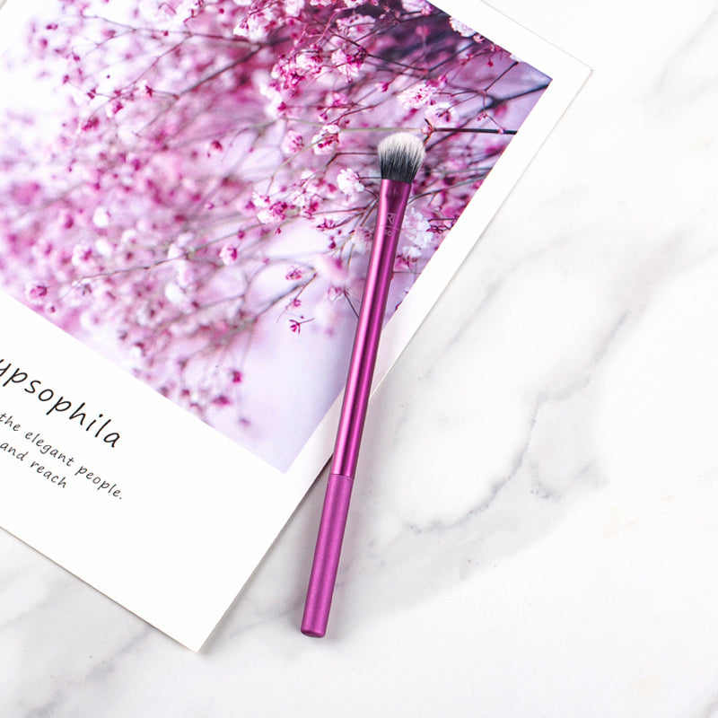 Purple makeup brush on a white surface with a floral background