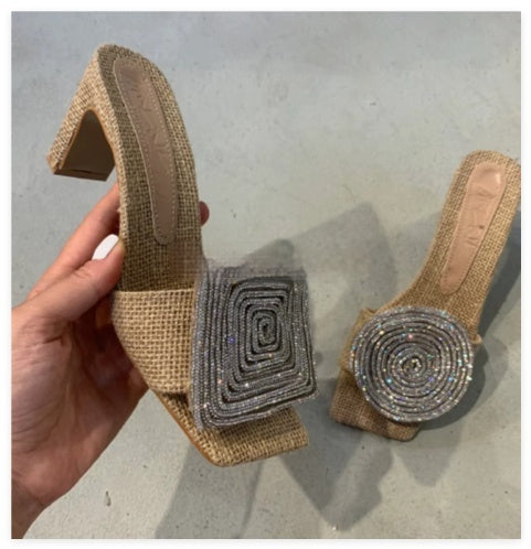 Beige high-heeled shoes with decorative silver embellishments on a gray surface