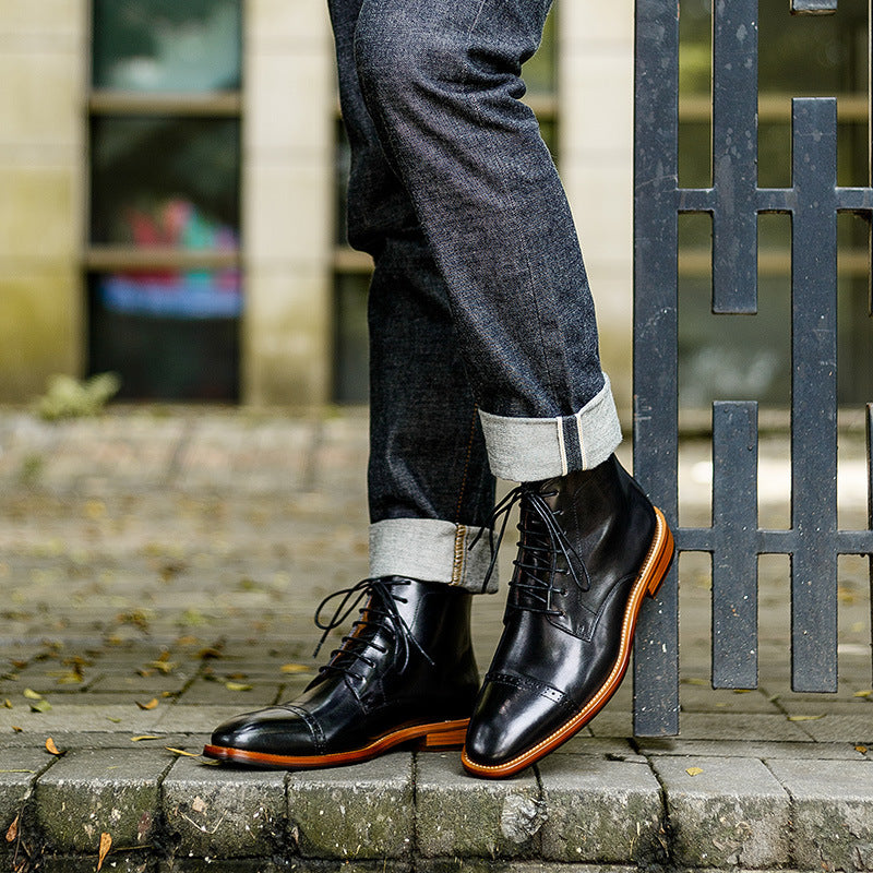 Person wearing black leather boots with orange soles standing on a stone pavement.