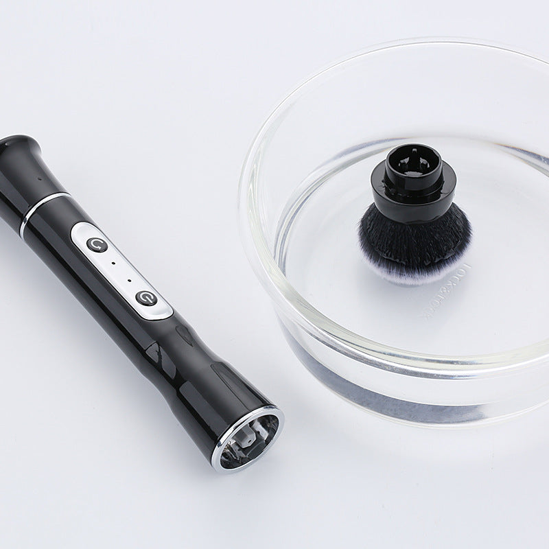 Black handheld cleaning tool with a brush attachment next to a clear glass bowl on a white background