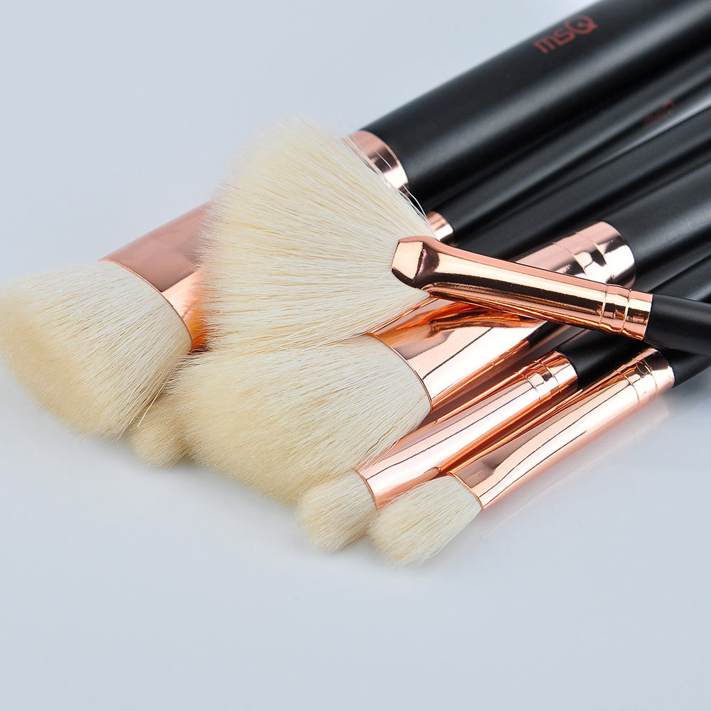 Set of makeup brushes with rose gold and black handles on a light gray background