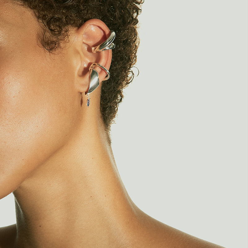 Close-up of a person wearing a silver earring with a clear gemstone on a neutral background
