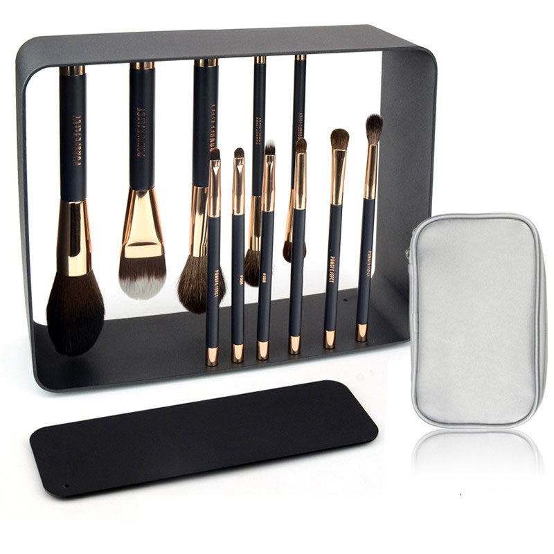 Set of makeup brushes with a black stand and silver case on a white background