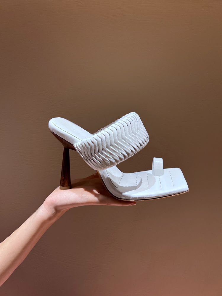 White high-heeled shoe held by a hand against a brown background