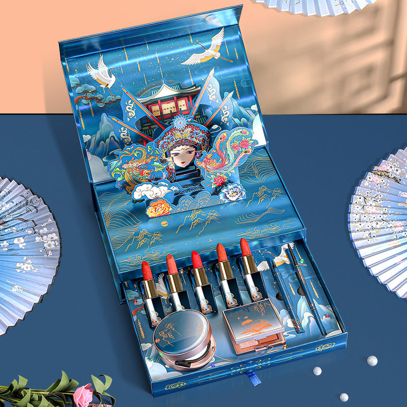 Makeup set with lipsticks and a compact mirror in an ornate blue box on a blue background.