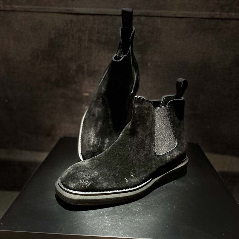 Pair of dark suede boots on a black surface with a neutral background