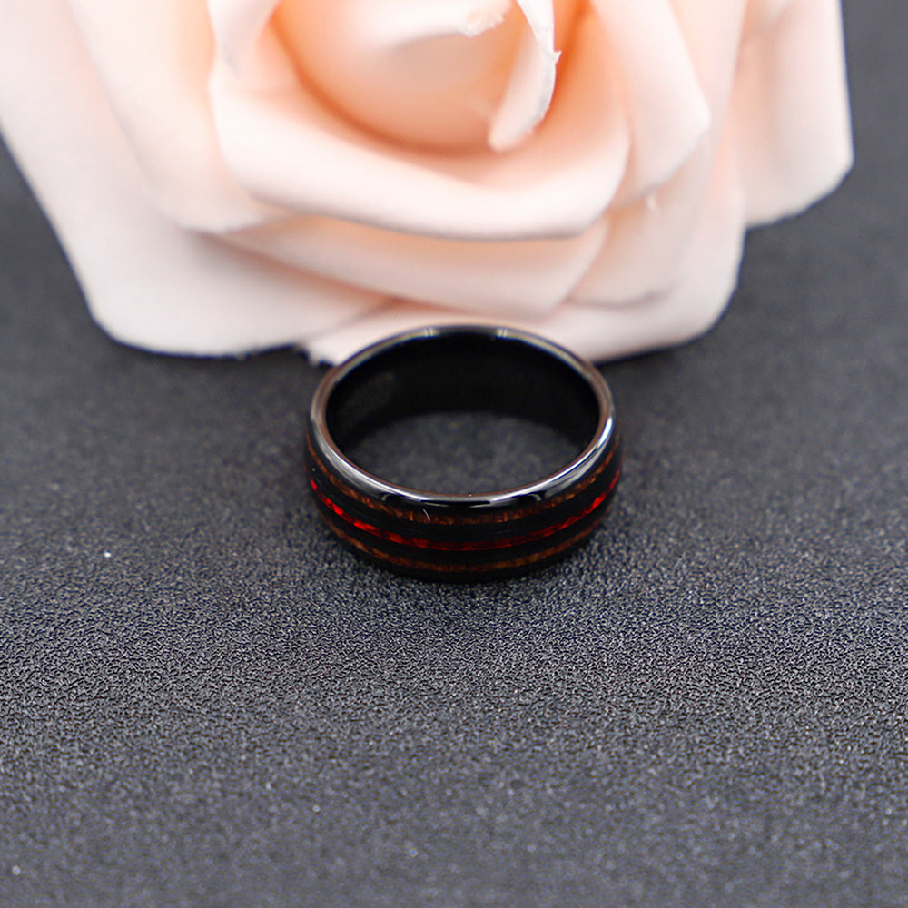 Black ring with red interior pattern on a gray surface with a white rose.
