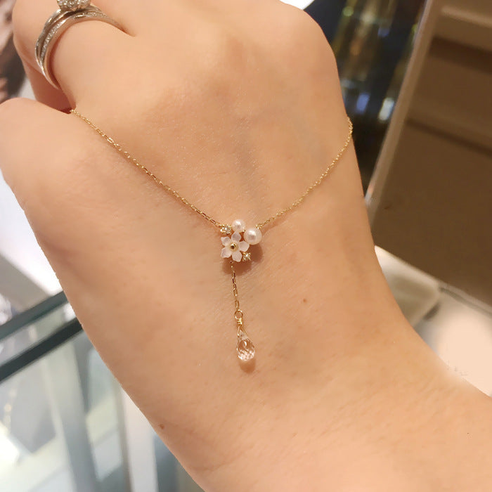 Gold anklet with floral charm on a wrist against a blurred background