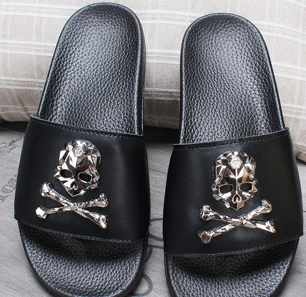 Black slides with gold skull and crossbones design on a neutral background