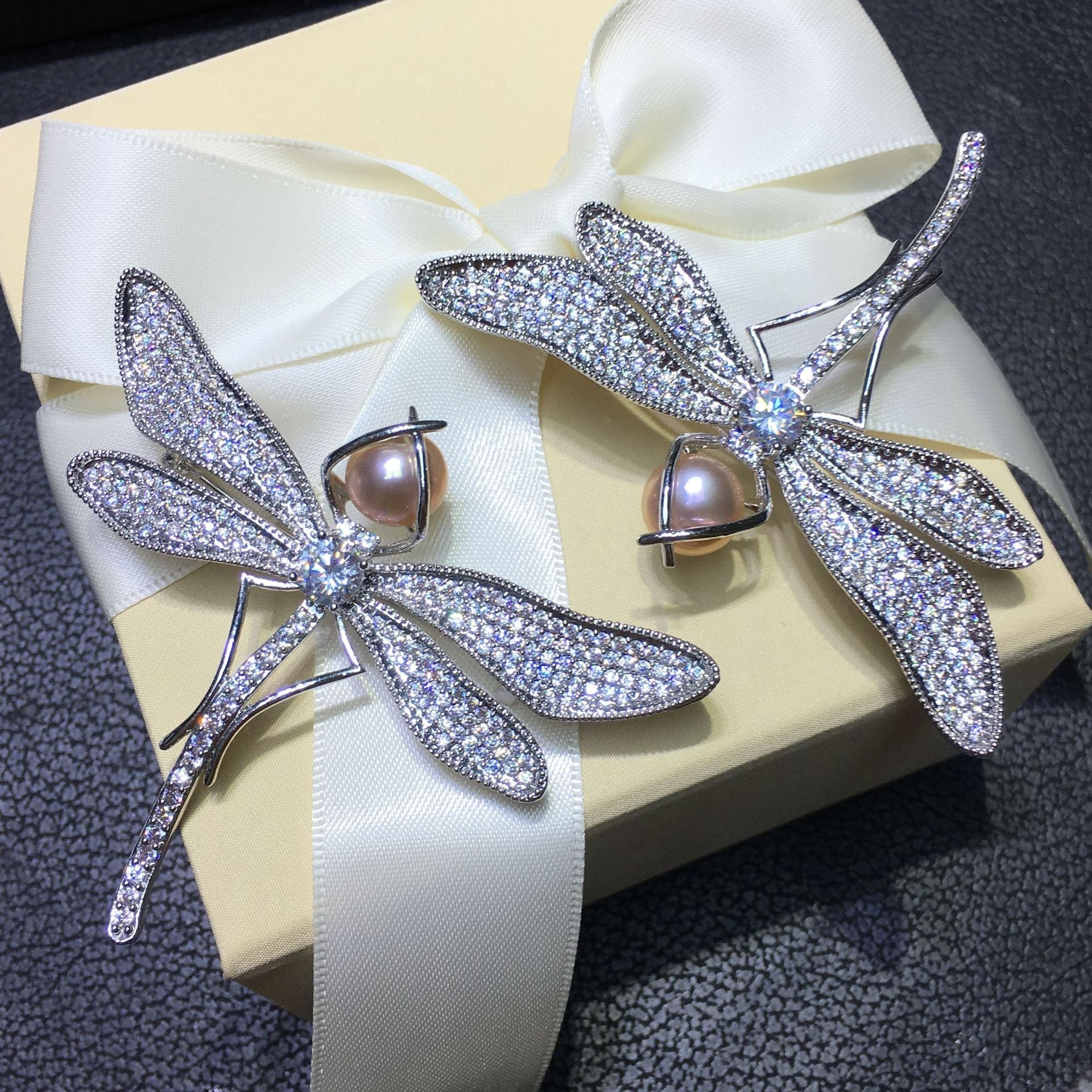 Dragonfly-shaped earrings with pearl centers on a decorative box with ribbon