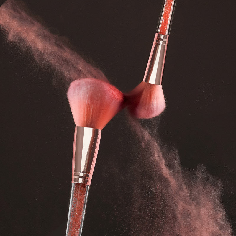 Makeup brushes with pink bristles and rose gold handles dusted with a pink powder against a black background.