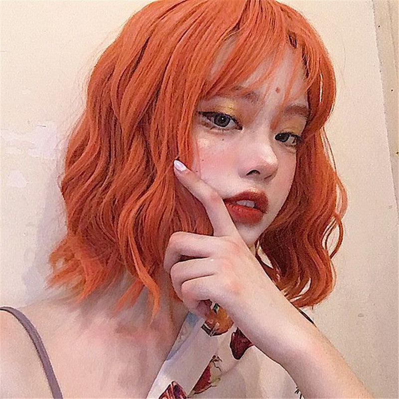 Person with vibrant orange hair posing with a hand on their chin against a neutral background
