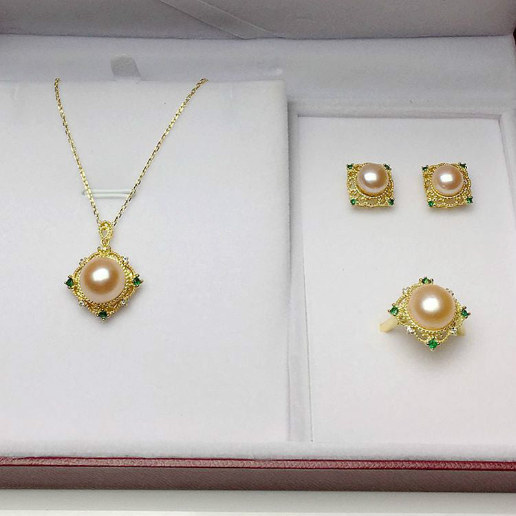 Pearl necklace and earrings set with gold and green accents on a white display box.