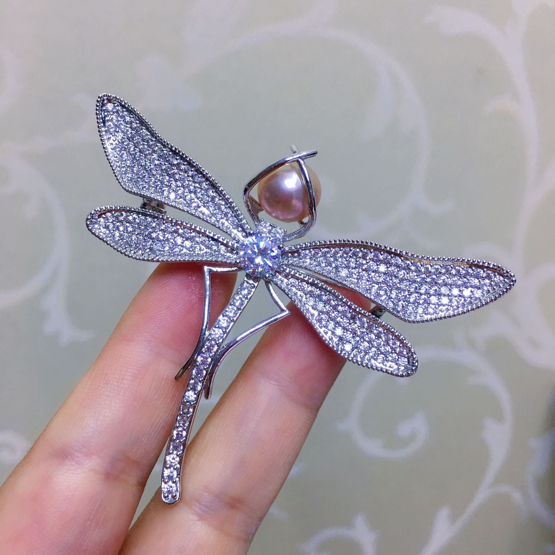 Silver dragonfly-shaped brooch with gemstones held by a hand against a light background