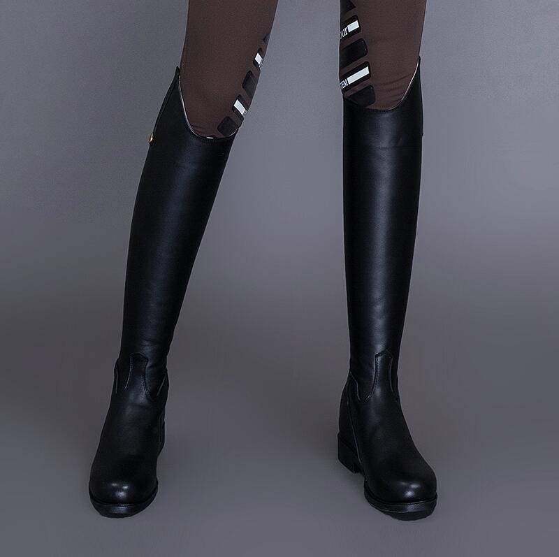 Black knee-high boots worn with brown pants on a gray background