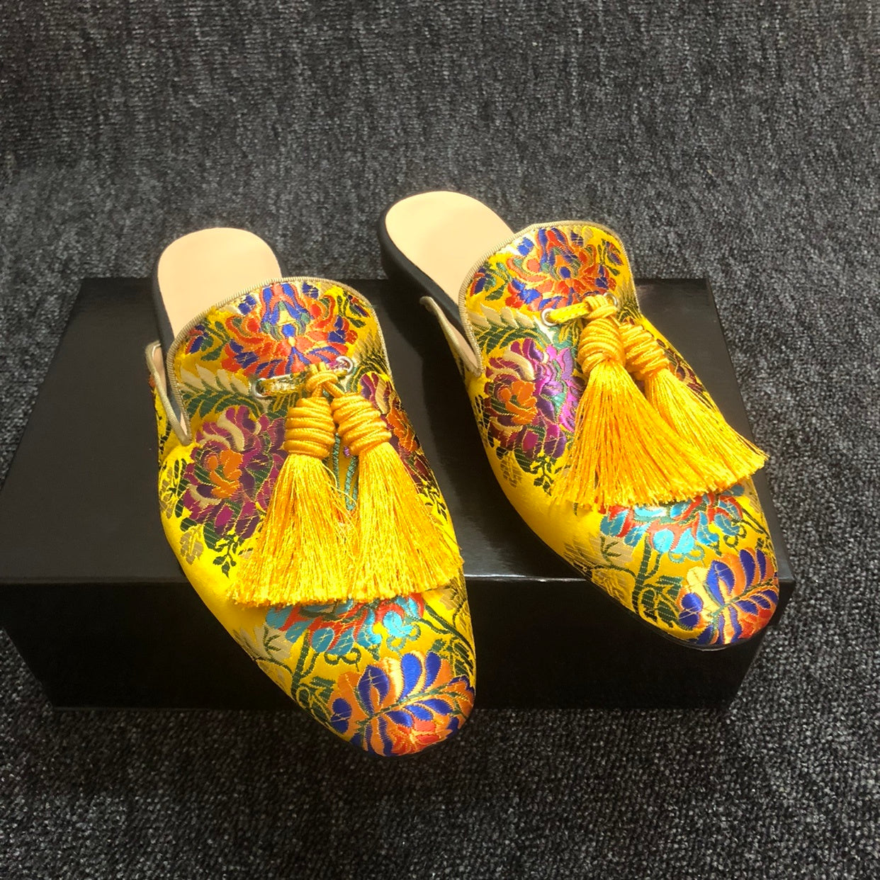 Pair of colorful embroidered slippers with tassels on a dark textured surface