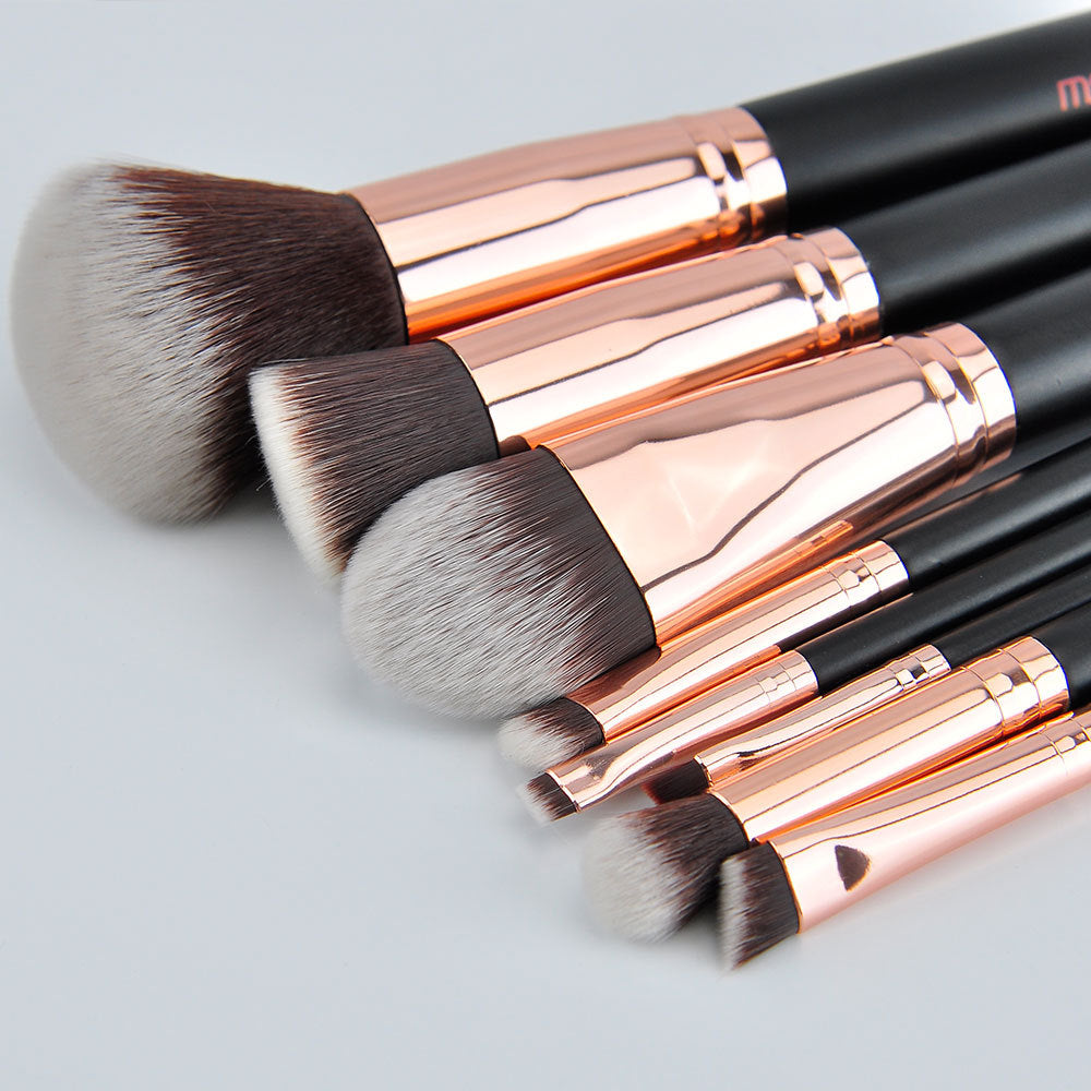 Set of makeup brushes with rose gold and black handles on a light gray background