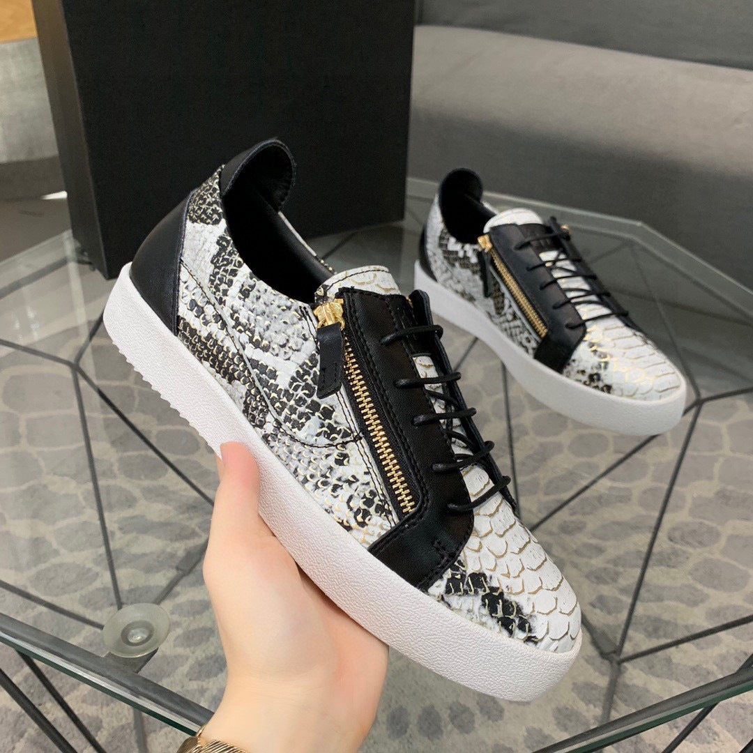 Snakeskin-patterned sneakers with a gold zipper held by a hand on a glass table.