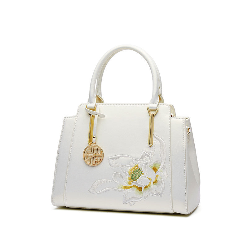 White handbag with floral design and gold accents on a white background