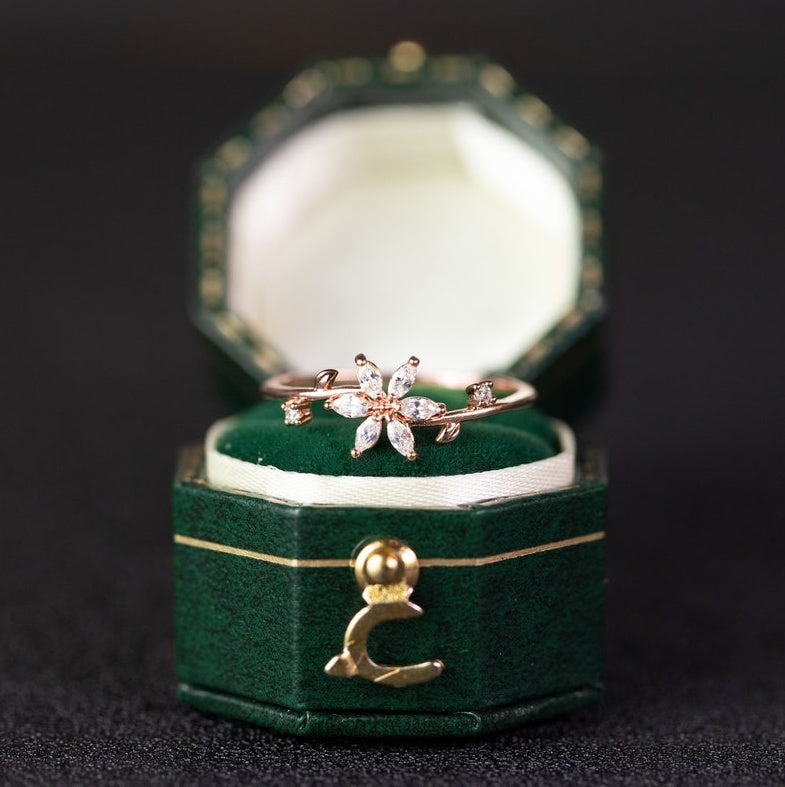 Gold ring with floral design in a green jewelry box on a dark background