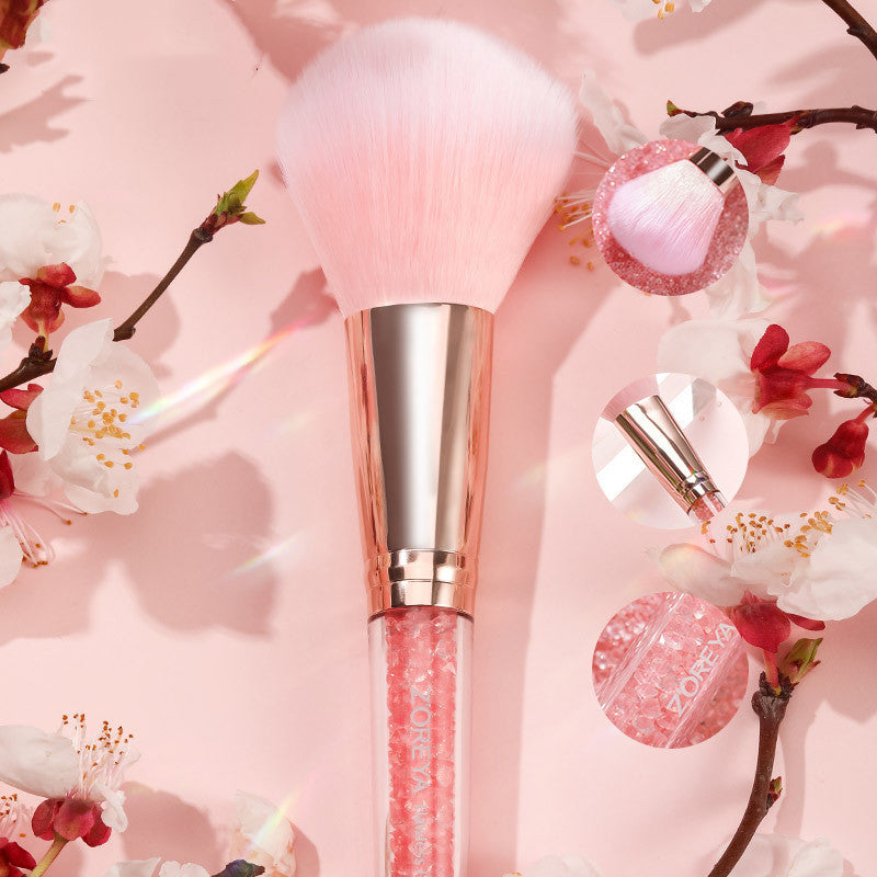 Makeup brush and lip gloss with cherry blossom branches on a pink background