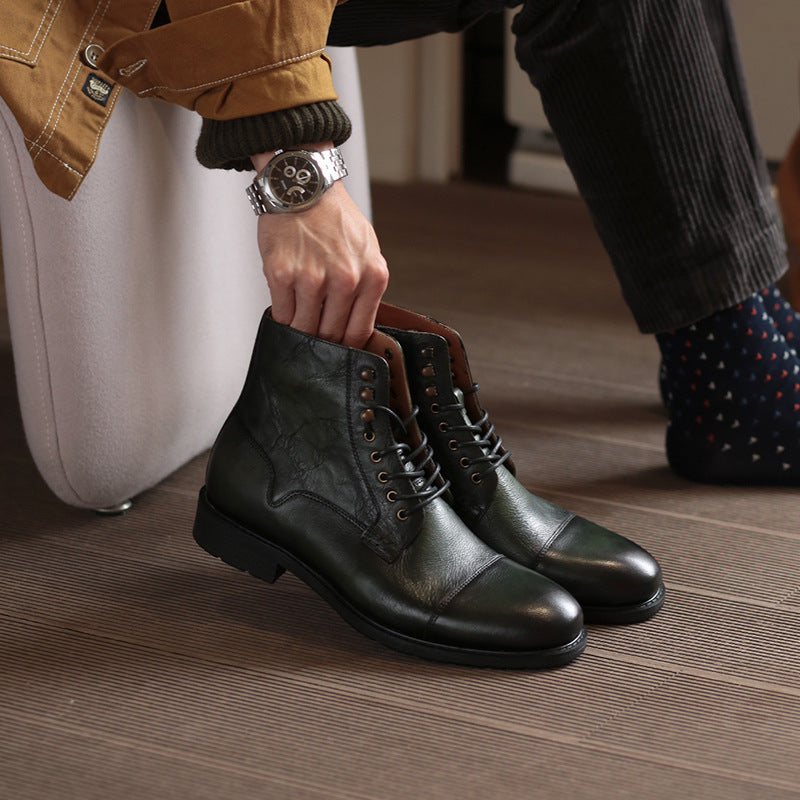 Person holding a pair of black leather boots on a wooden floor.
