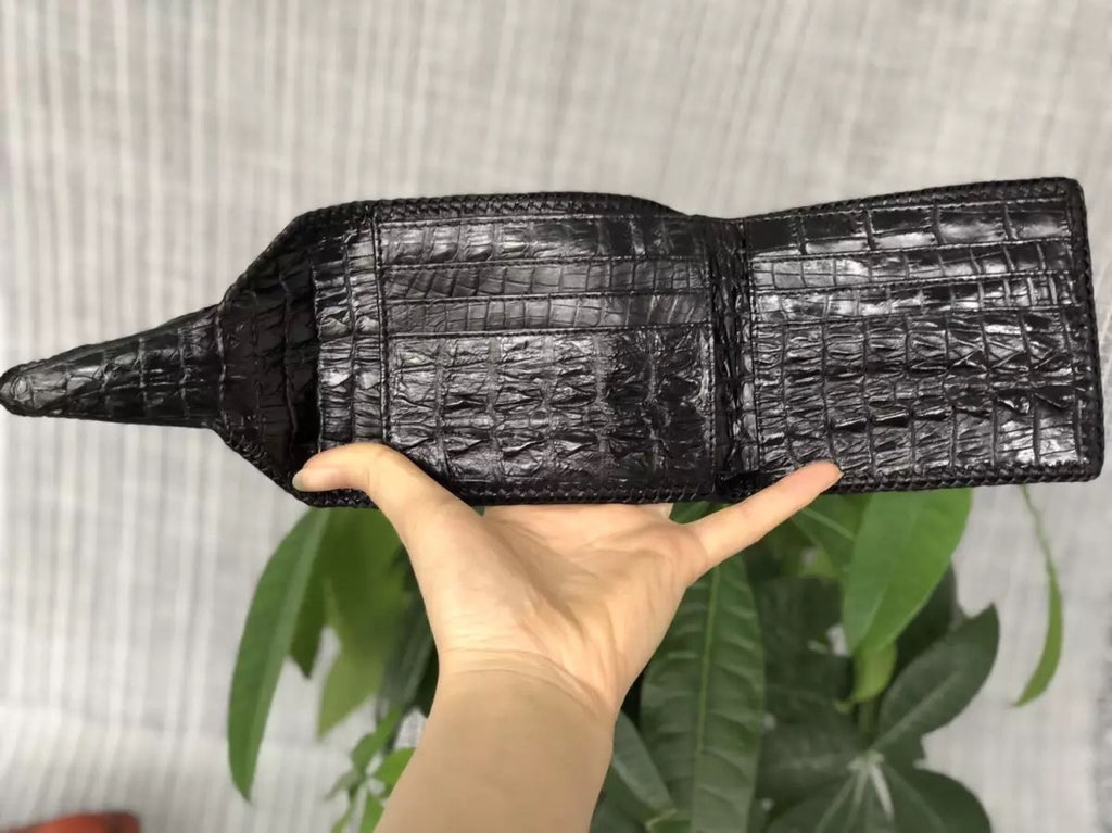 Black crocodile skin wallet held by a hand with a light gray background