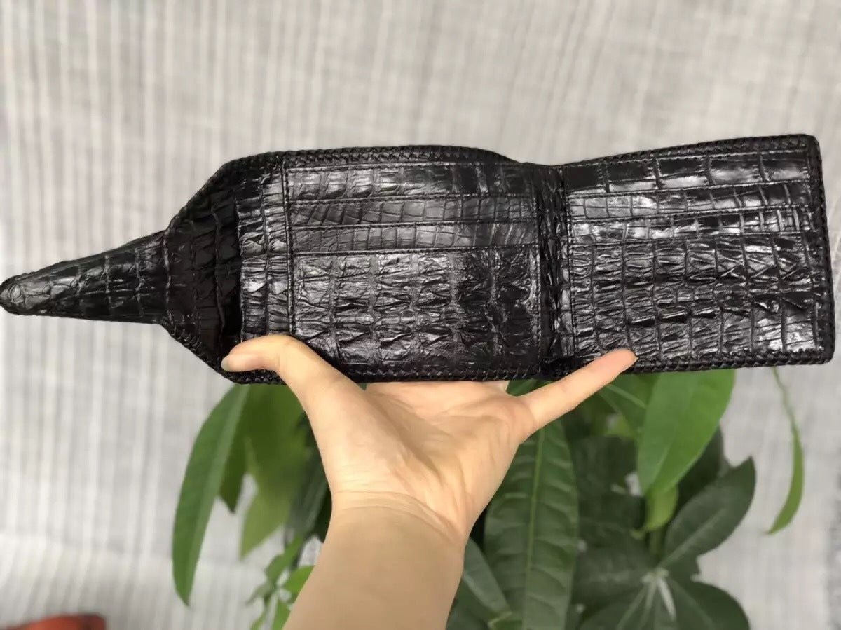 Black crocodile skin wallet held by a hand with a light gray background