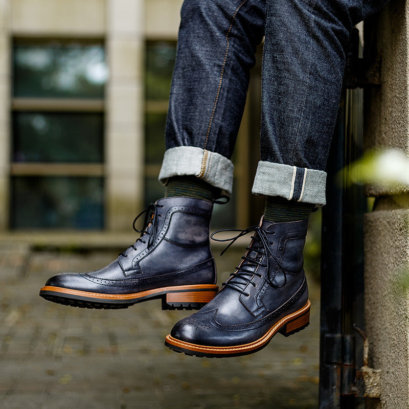 Person wearing dark blue leather boots with orange soles, standing on a ledge.