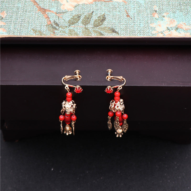 Pair of earrings with red beads and gold accents on a dark surface.