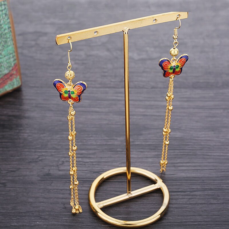 Butterfly earrings with gold chains on a stand against a dark background