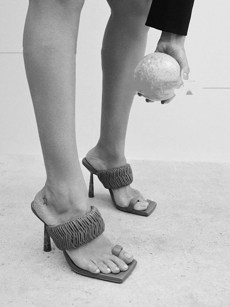 Black and white photo of feet wearing high-heeled sandals with textured straps on a light background.