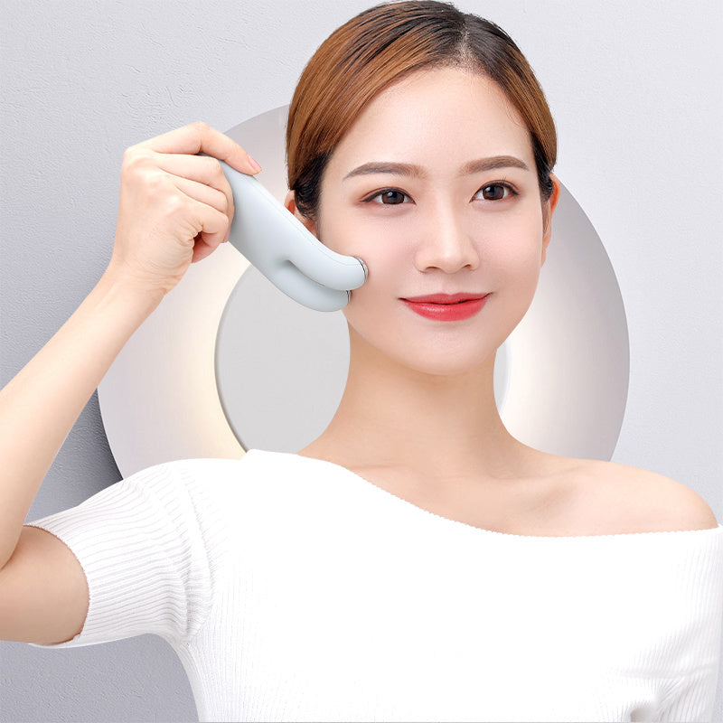 Woman using a white handheld device on her face against a light gray background