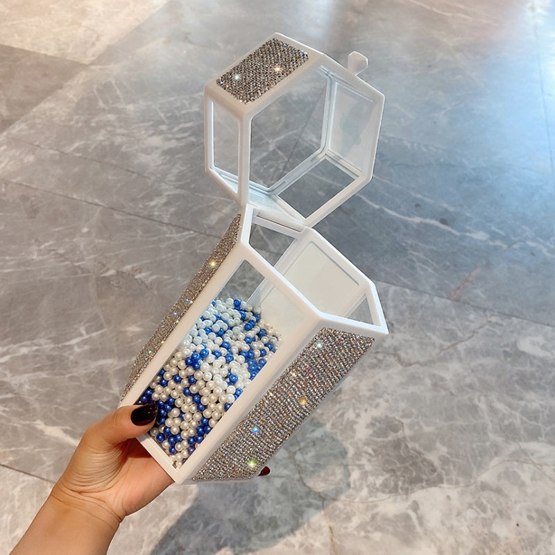 Transparent geometric handbag with rhinestone accents held by a hand on a marble surface