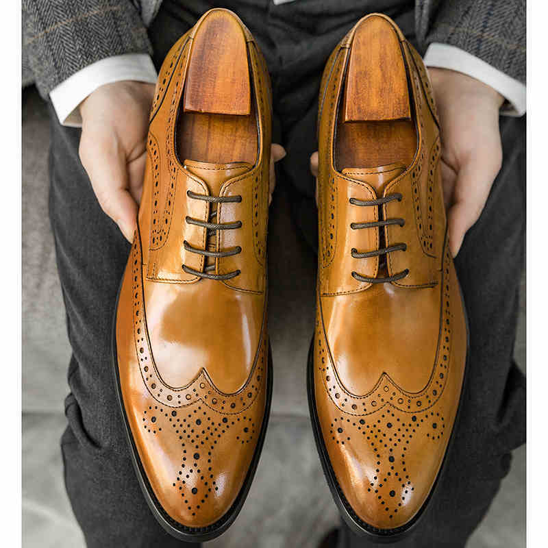 Pair of brown leather dress shoes with wooden soles held by a person.