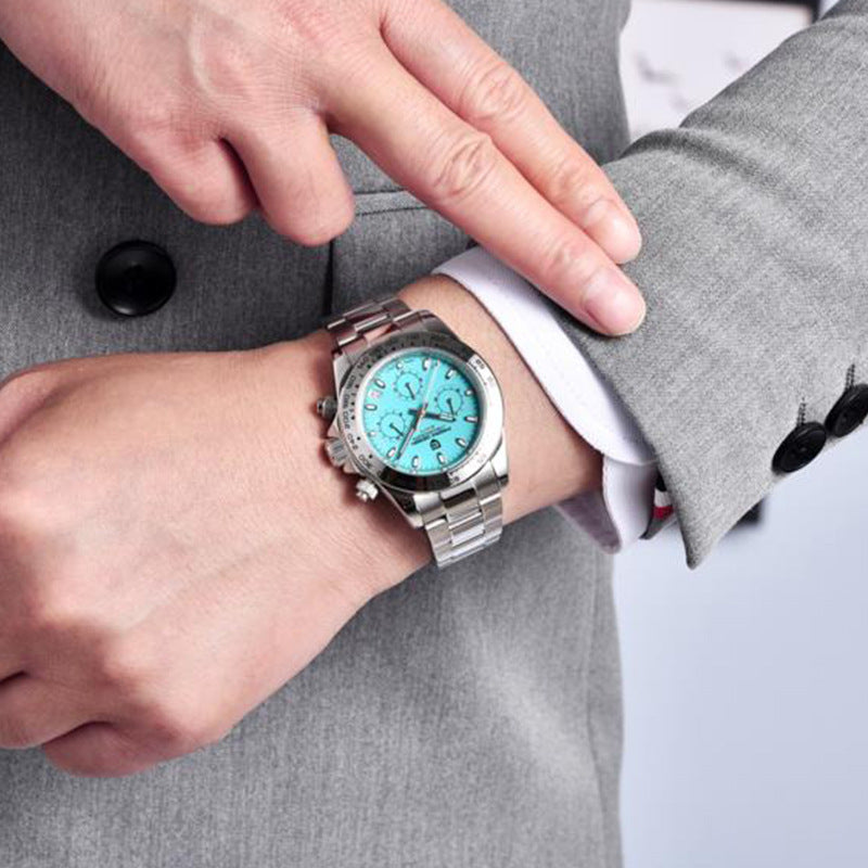 Person wearing a silver watch with a turquoise face on a gray suit background