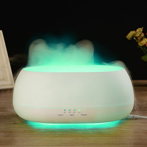 White essential oil diffuser emitting mist on a wooden surface with a dark background