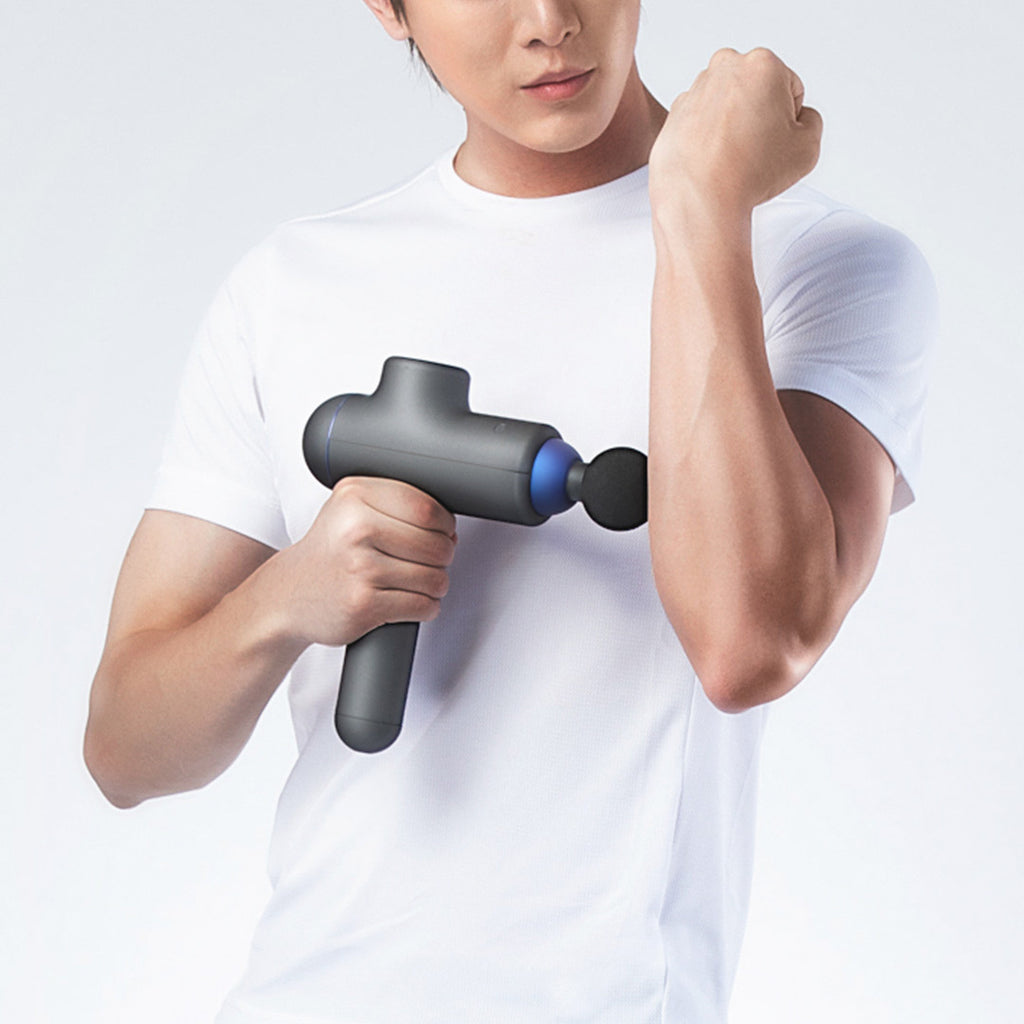 Person using a handheld massage gun on their arm against a white background