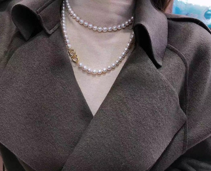 Person wearing a pearl necklace with a dark coat