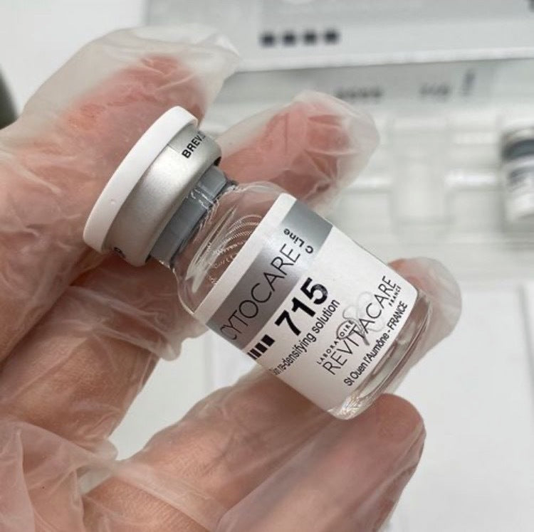 Hand holding a Revitacare 715 vial with a glove on a blurred background