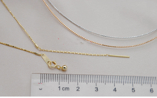 Gold necklace with a clasp on a gray surface with a ruler for scale.
