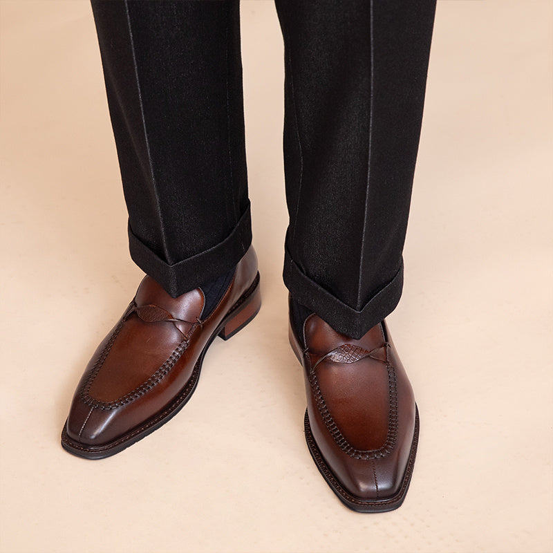 Brown dress shoes worn with black pants on a beige background