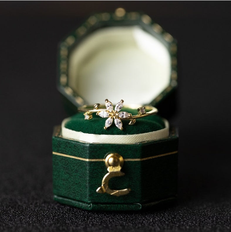 Gold ring with floral design in a green jewelry box on a dark background