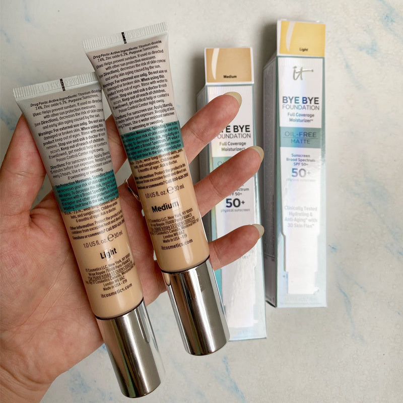 Two tubes of foundation held by a hand with packaging in the background.