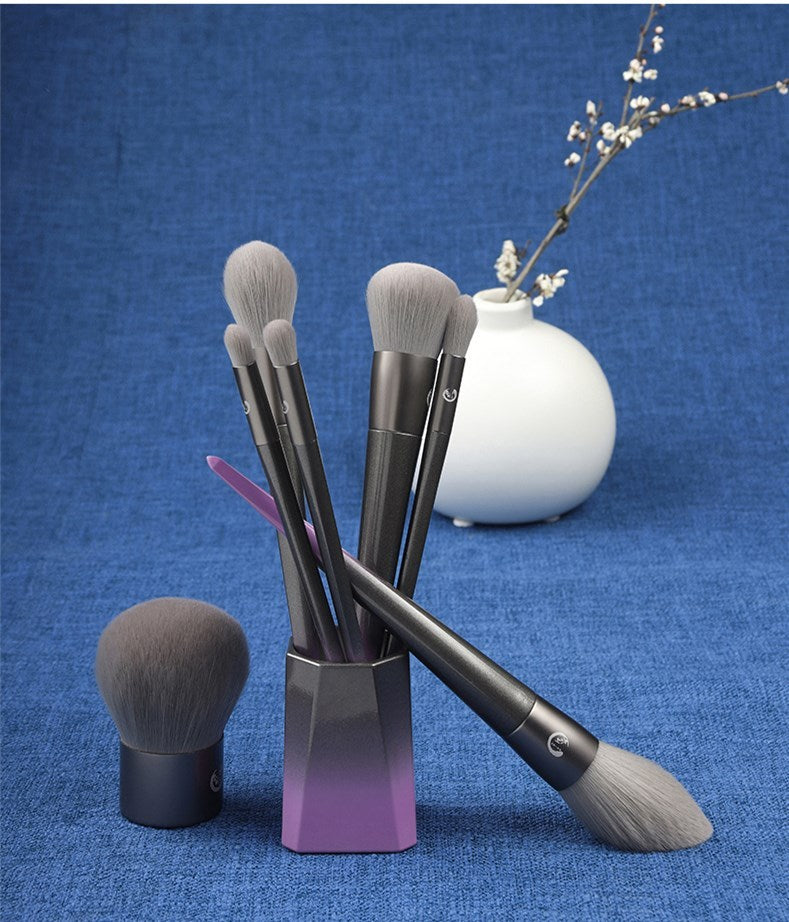 Set of makeup brushes in a holder on a blue background with a white vase and branch.