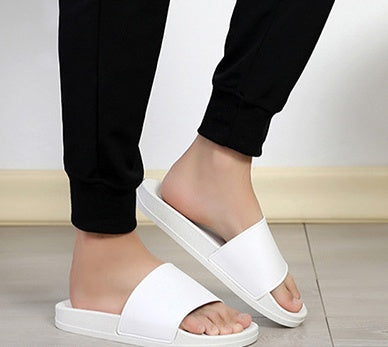 White sandals worn with black pants on a light wooden floor.