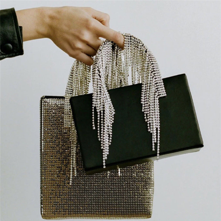 Black clutch with chain strap held by a hand against a light gray background