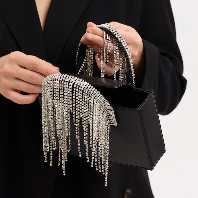 Black handbag with silver fringe details held by a person wearing a black coat.