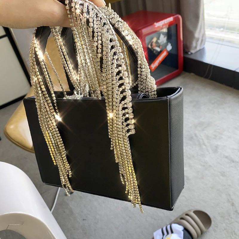 Black handbag with gold chain strap held by a person indoors.